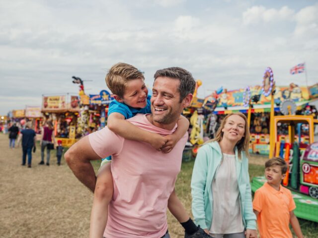 Family enjoying time at the fairground. Dad is carrying his son on his back