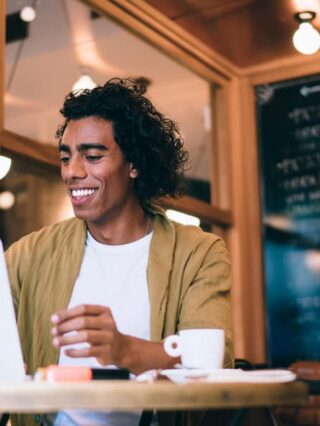 Cheerful man reading emails on his laptop working remotely in a cafe in Spain