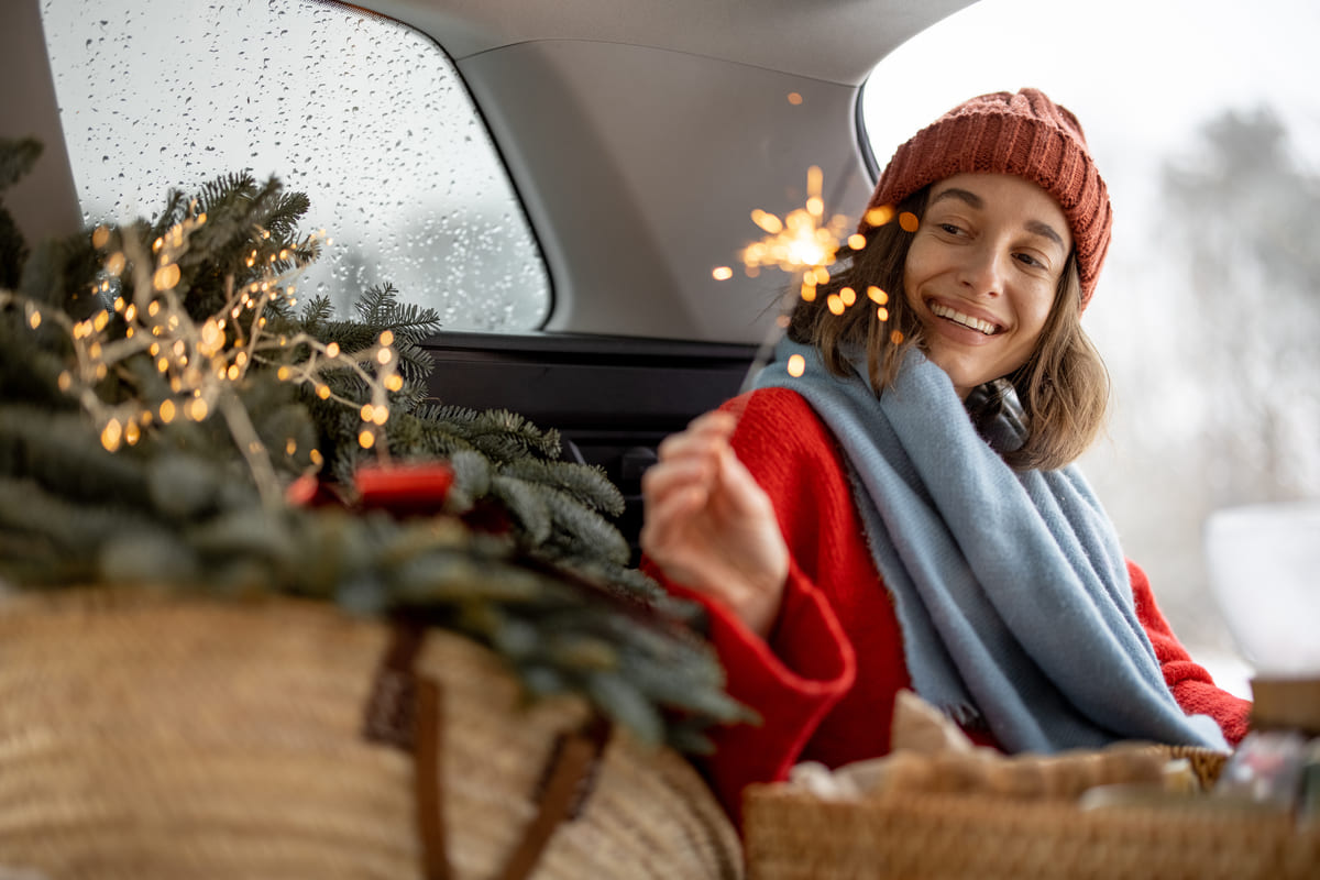 William Russell Blog -How to Survive Lonely Christmas Abroad as an Expat - Woman smiling and looking at sparkler while sitting in car trunk