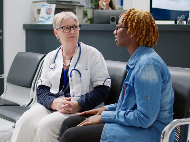 Senior physician consulting woman in waiting room lobby