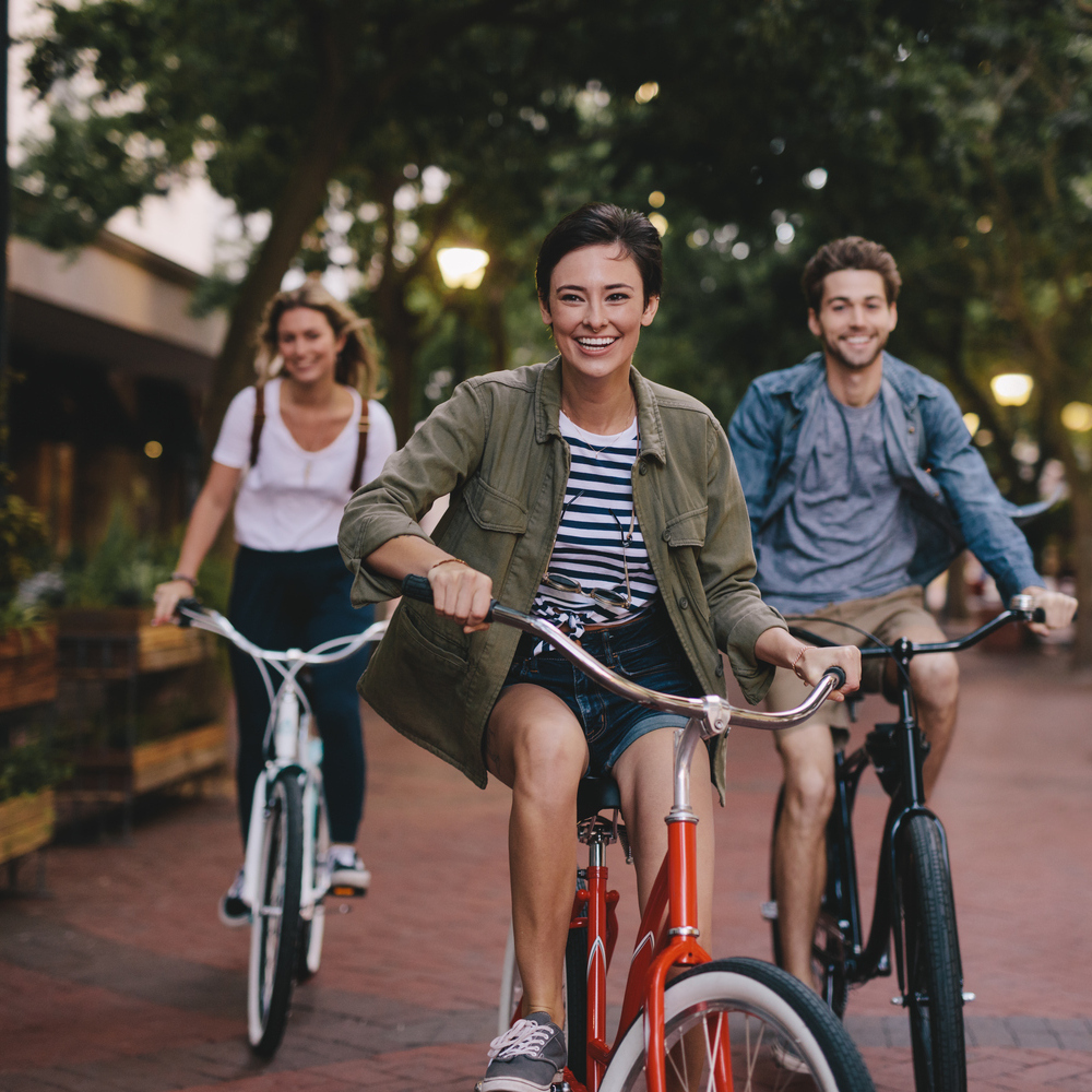 Two young women and a young man cycling down a street together on bikes looking very happy