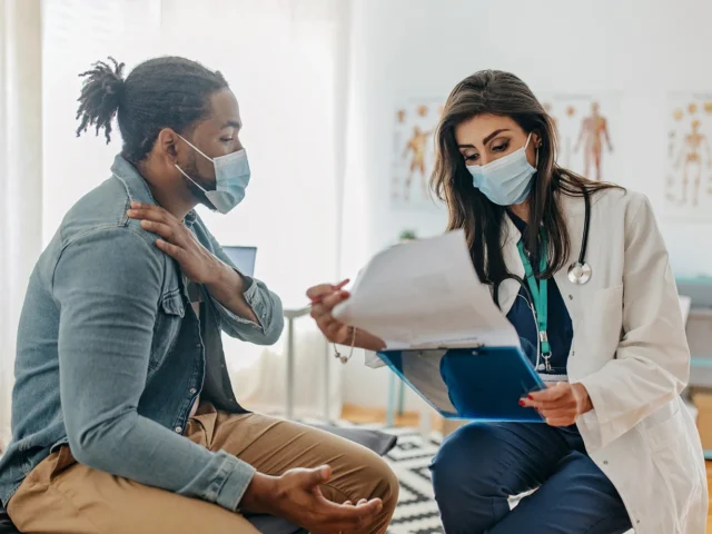 Male patient and female doctor that is providing medical assistance. They are sitting at the medical table and discuss symptoms