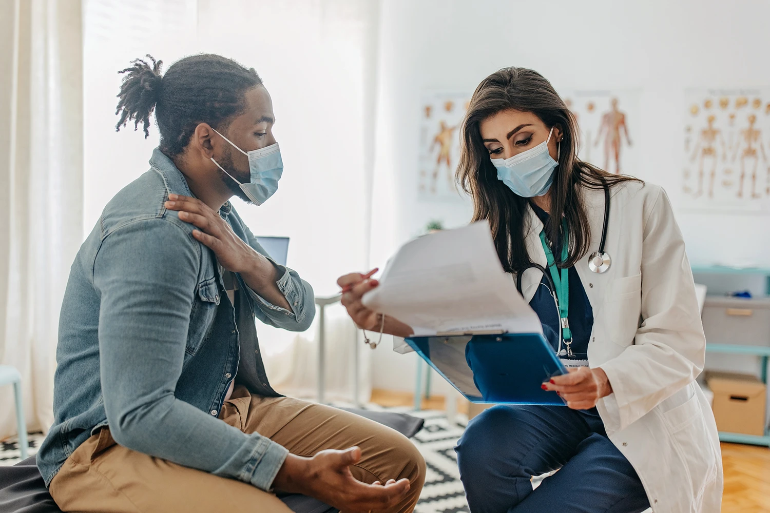 Male patient and female doctor that is providing medical assistance. They are sitting at the medical table and discuss symptoms
